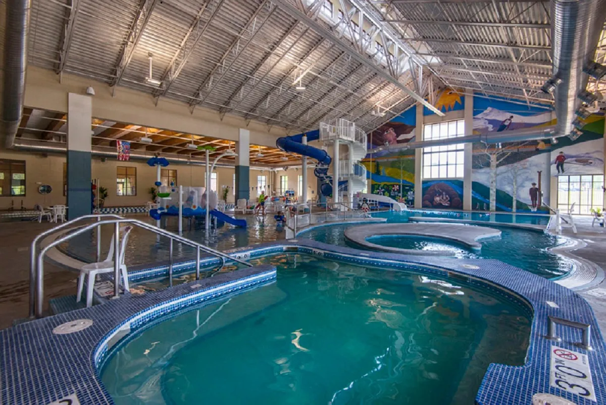 This image features a swimming pool area with a water slide, children playing in the water, and a colorful mural on the wall. The atmosphere is lively and joyful, highlighting a family-friendly recreational space perfect for kids and parents alike.