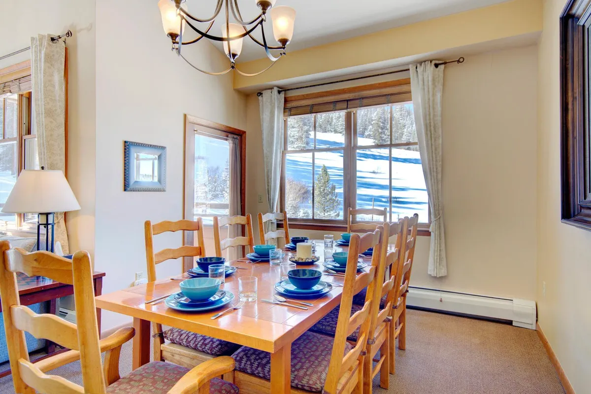 A spacious dining area with a large table set beneath an elegant chandelier, framed by a large window that provides scenic mountain or village views. The room radiates warmth and is ideal for shared meals and celebrations.