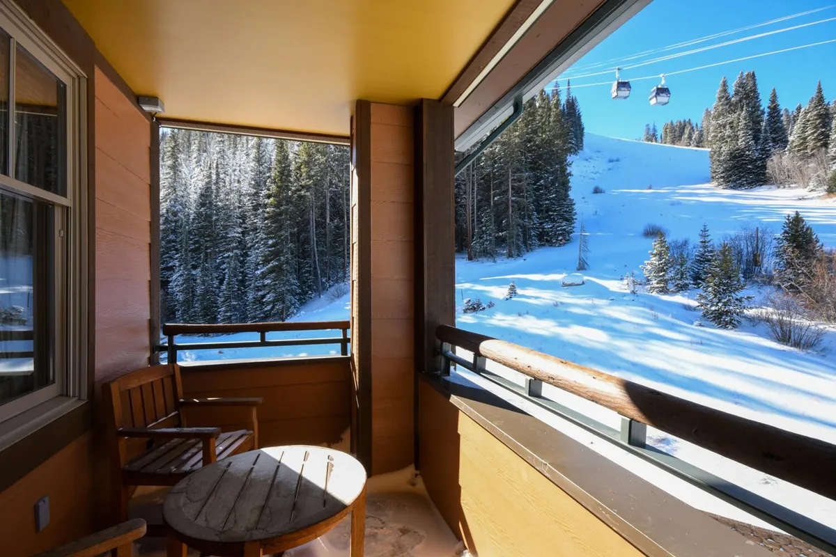 A serene private deck set with wooden chairs and a round table, overlooking a snowy mountain landscape and passing cable cars. The scene invites relaxing with a warm drink while soaking in the mountain views.