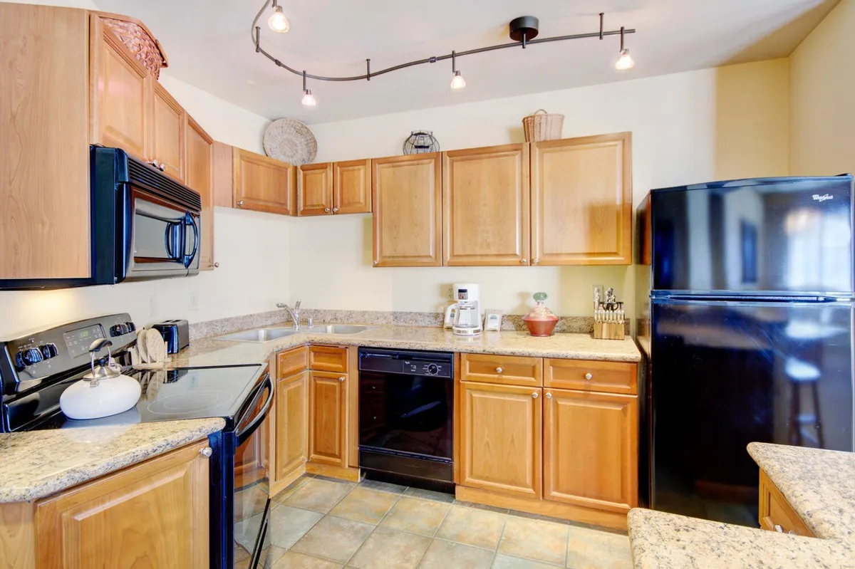 A modern, fully equipped kitchen with granite countertops, sleek black appliances, wooden cabinets, and track lighting. The space is inviting and designed for both casual breakfasts and gourmet meal preparation.