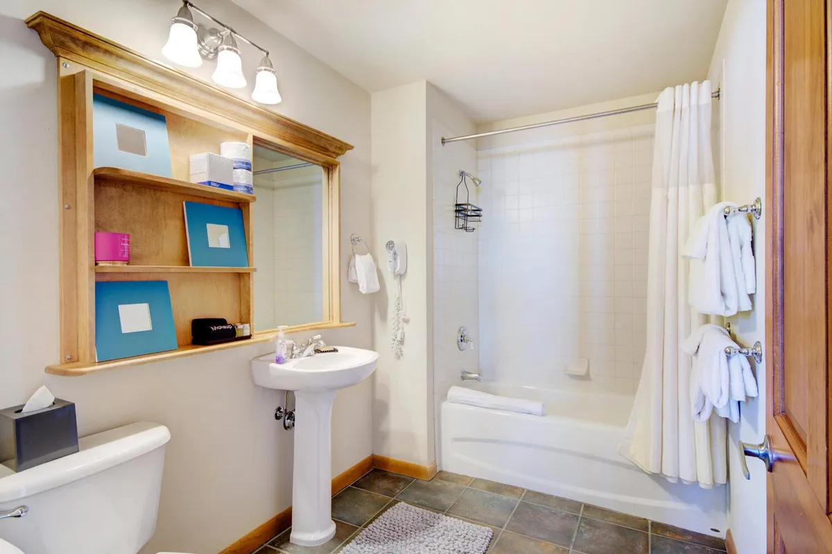 A calming bathroom with a pedestal sink, inviting bathtub, open shelving with neatly arranged organic toiletries, and a mirror. The atmosphere is refreshing and soothing, perfect for self-care routines or unwinding in a warm bath.