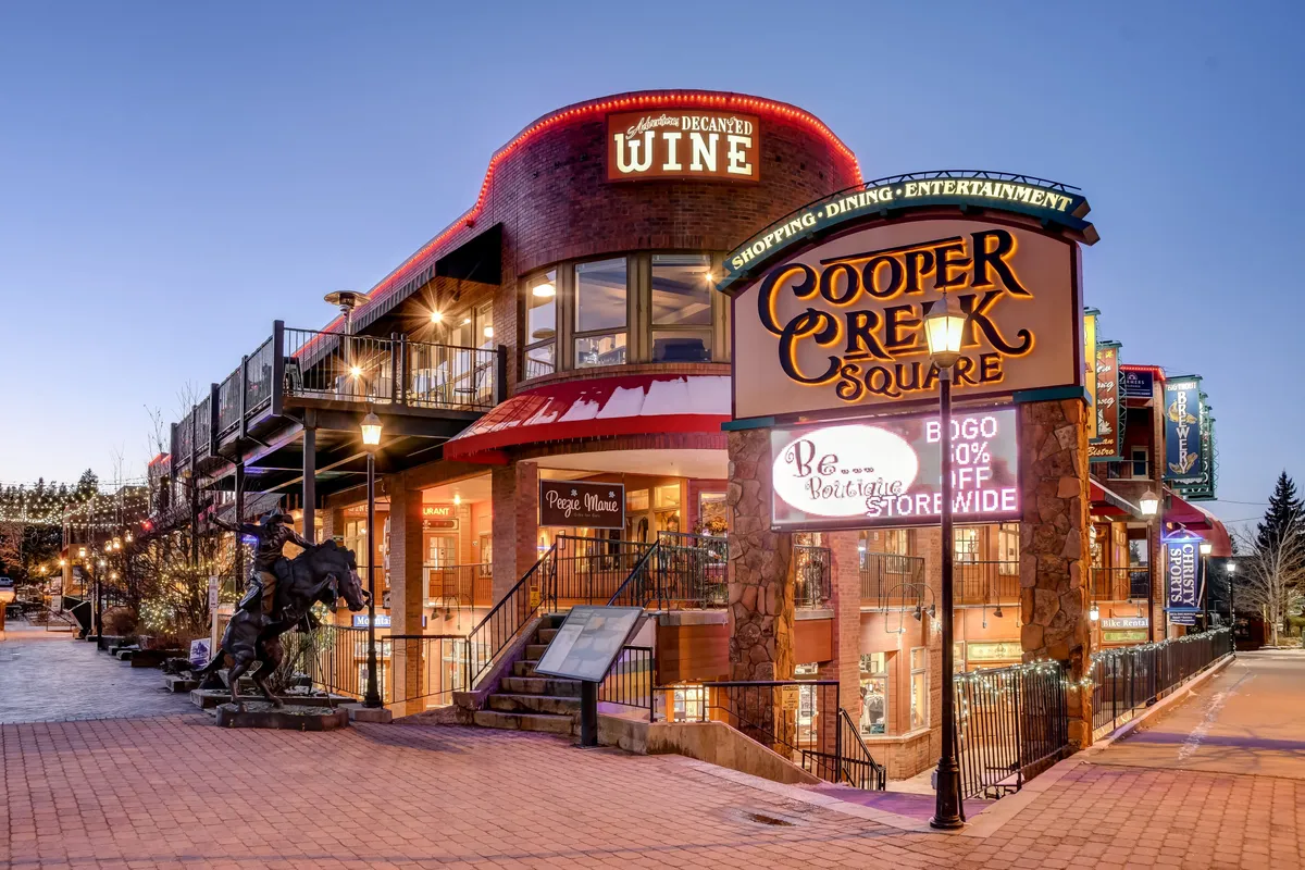 An exterior shot of Cooper Creek Square, featuring decorative architecture, clear signage for shopping and wine, and hints of bustling activity. The mood is lively and welcoming, suggesting vibrant community life and easy access to local dining and entertainment.