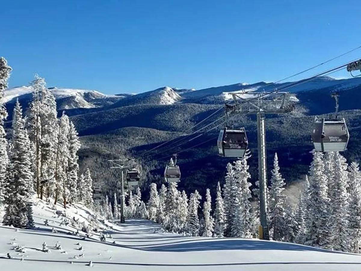 This image captures ski lift gondolas gliding above snow-covered trees with a dramatic mountain range in the background. The setting is serene yet adventurous, showcasing both the excitement of hitting the slopes and the beauty of Winter Park's natural environment.