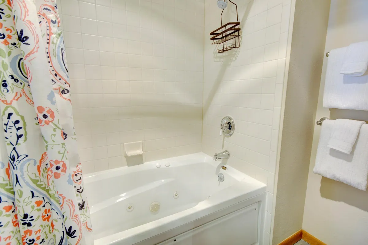 A tranquil bathroom scene showcasing a whirlpool tub with a colorful shower curtain and neatly stacked towels, inviting relaxation after a day of activity.