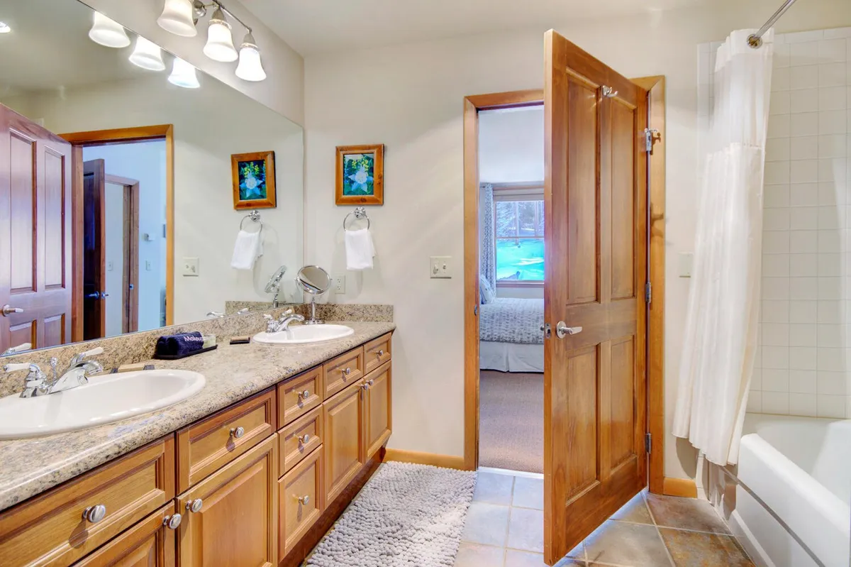 A spacious bathroom featuring a double sink vanity, a large mirror, wooden cabinetry, and decorative art frames. The ambiance is calm and serene, suggesting a spa-like experience suitable for soothing routines and relaxation.
